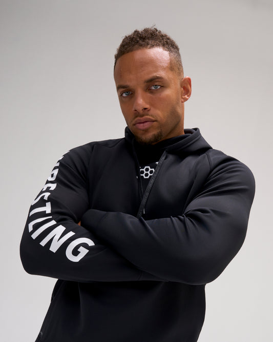 Male athlete wearing the black RUDIS Wrestling COOL-FEEL Hoodie with arms crossed, showcasing the bold white WRESTLING sleeve graphic.