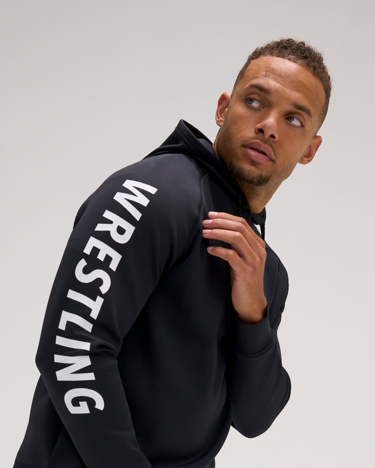 Male athlete wearing the black RUDIS Wrestling COOL-FEEL Hoodie, featuring a close view of the bold white WRESTLING sleeve graphic.
