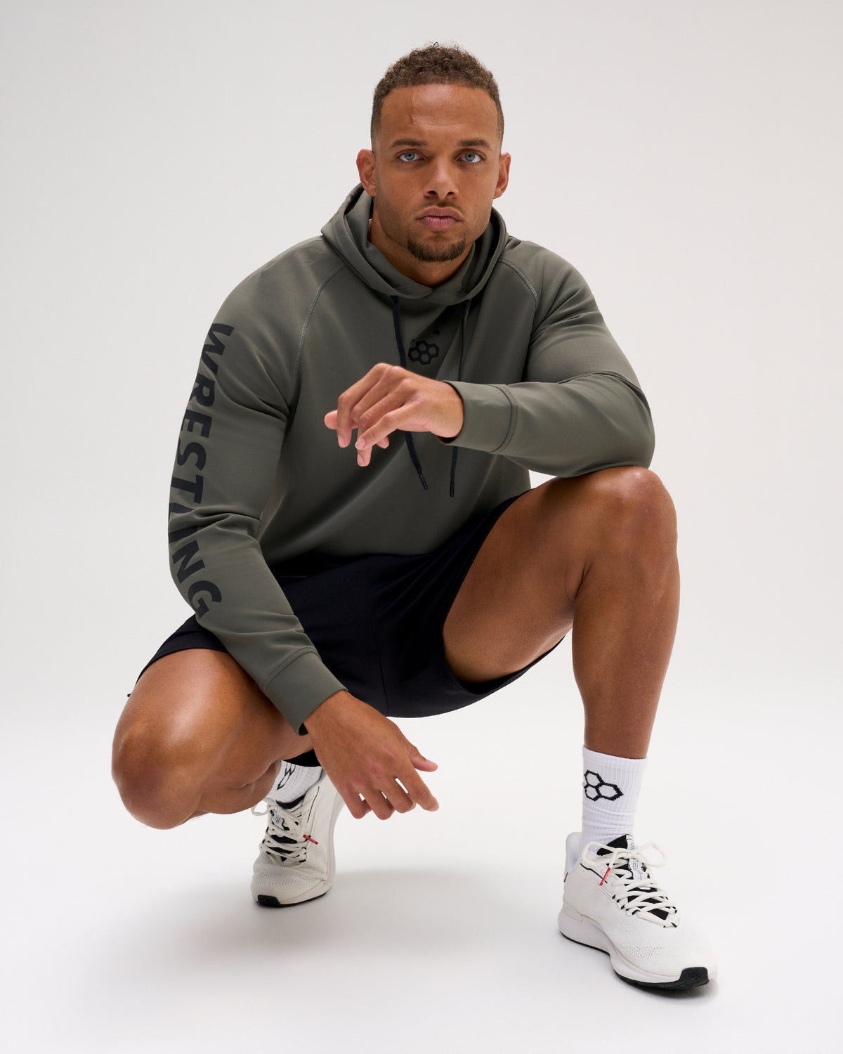 Male athlete wearing the dark olive RUDIS Wrestling COOL-FEEL Hoodie with black shorts, showcasing the chest mark and WRESTLING sleeve graphic.