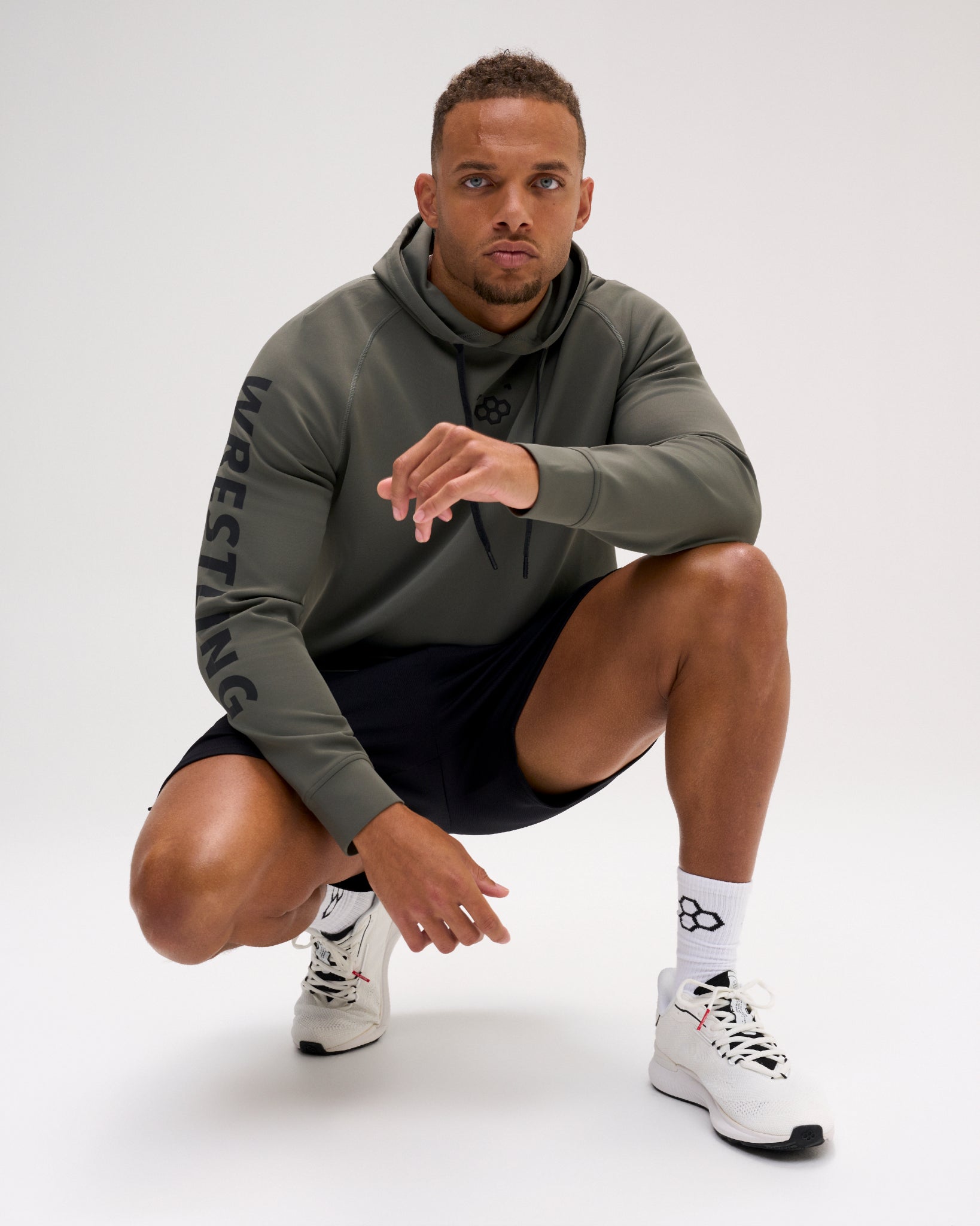 Male athlete wearing the dark olive RUDIS Wrestling COOL-FEEL Hoodie with black shorts, showcasing the chest mark and WRESTLING sleeve graphic.