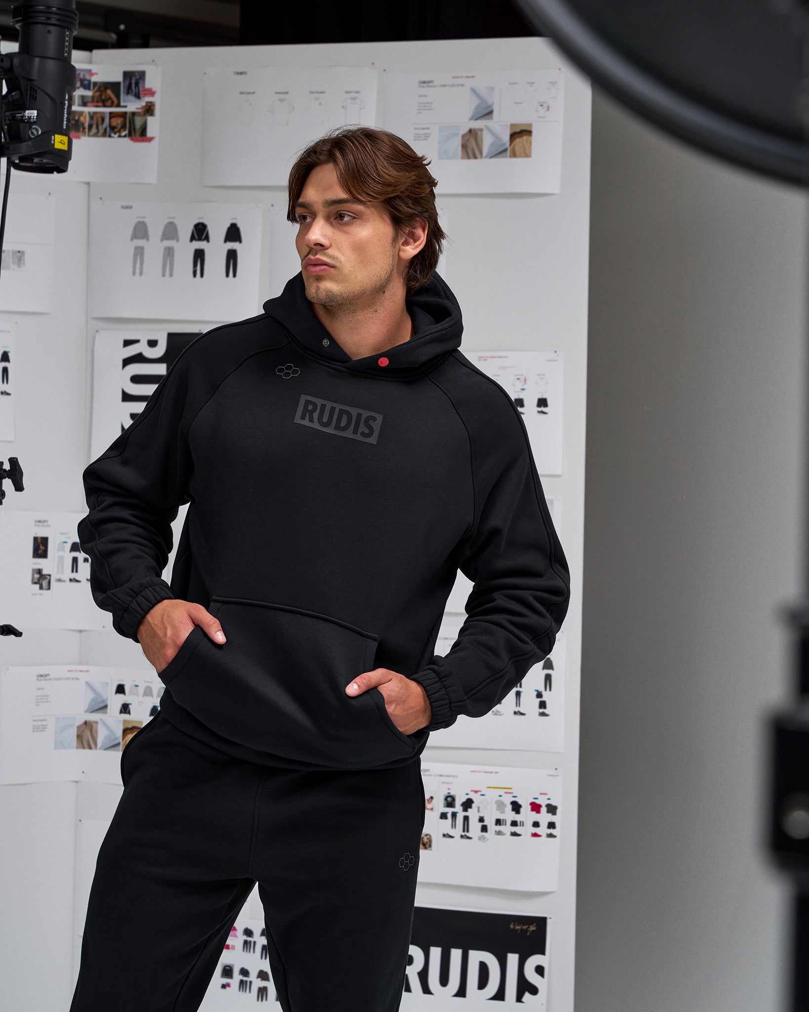 Person wearing a black hoodie with 'RUDIS' branding in a studio setting.