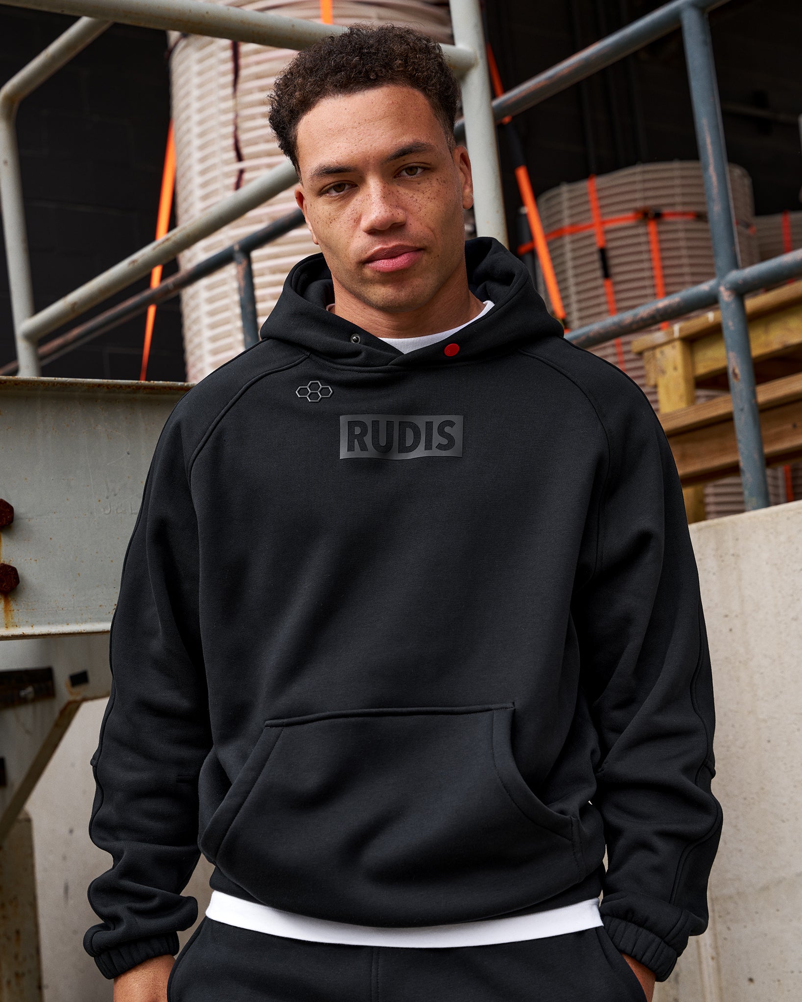 Person wearing a black hoodie with 'RUDIS' logo in an industrial setting