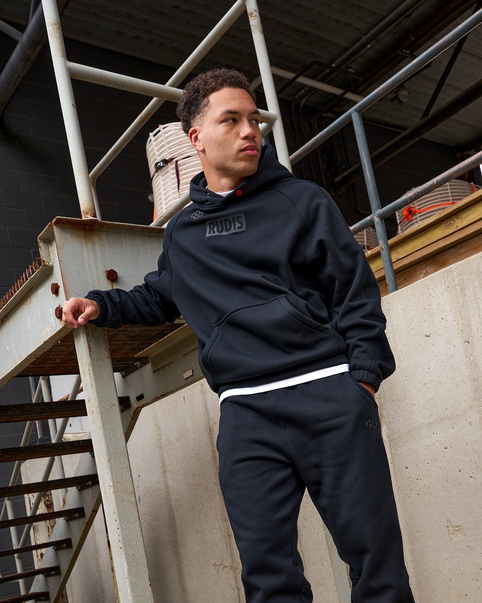 Person wearing a dark hoodie and pants standing on a metal staircase.