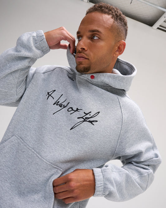 Model wearing the heather gray RUDIS A Way of Life Tech Fleece Hoodie, highlighting the script chest graphic, structured hood, and kangaroo pocket.