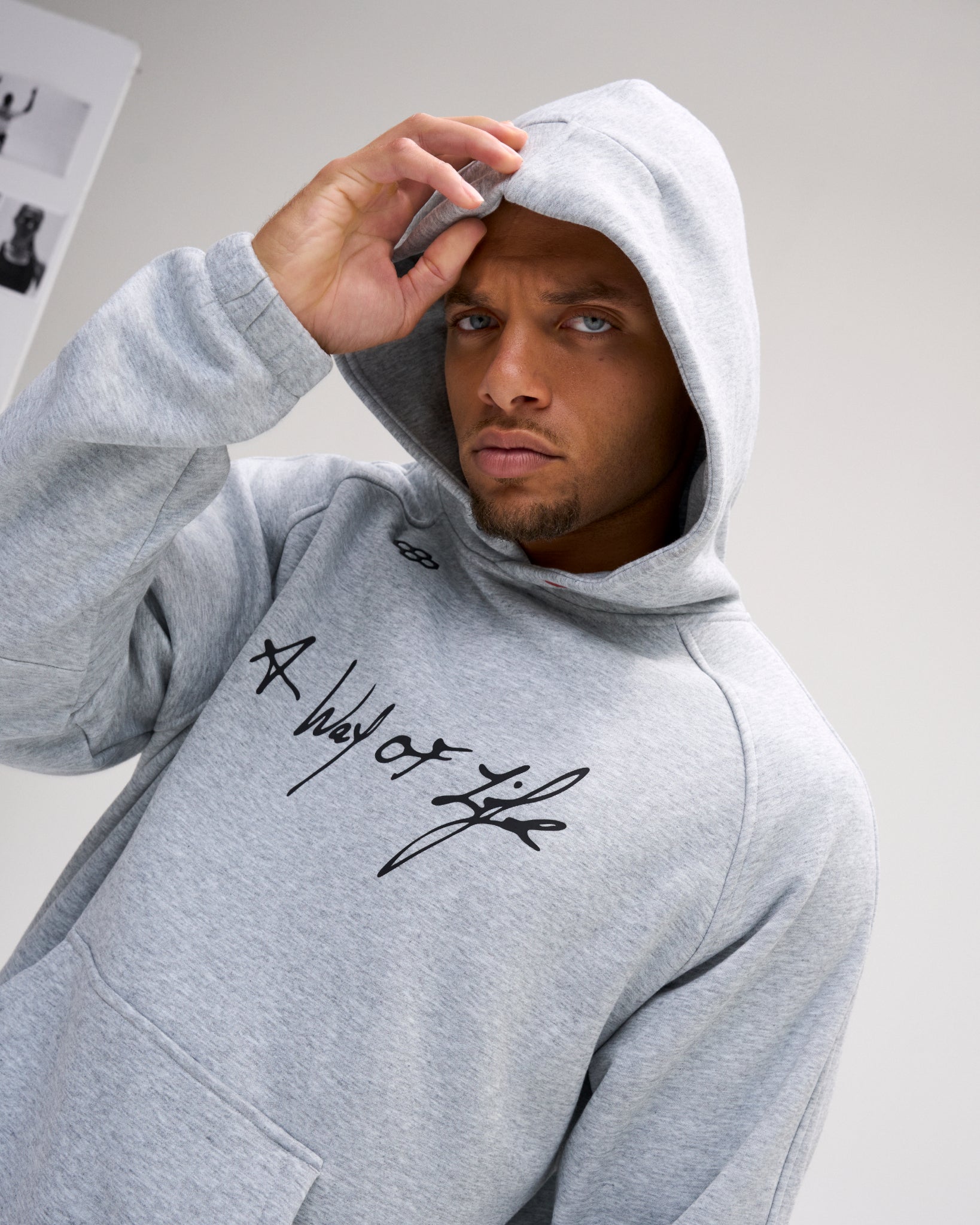 Model wearing the heather gray RUDIS A Way of Life Tech Fleece Hoodie with the hood up, showcasing the black script chest graphic and RUDIS mark.