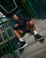 Person sitting on a staircase wearing black hoodie, shorts, and sneakers with white socks.