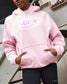 Person wearing a pink hoodie with 'All In' text, standing against a metal railing.