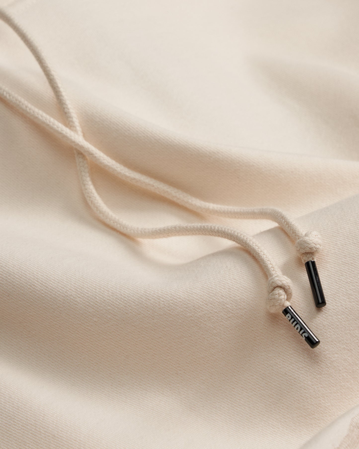 Close-up of a beige hoodie with a drawstring and brand logo on a beige background