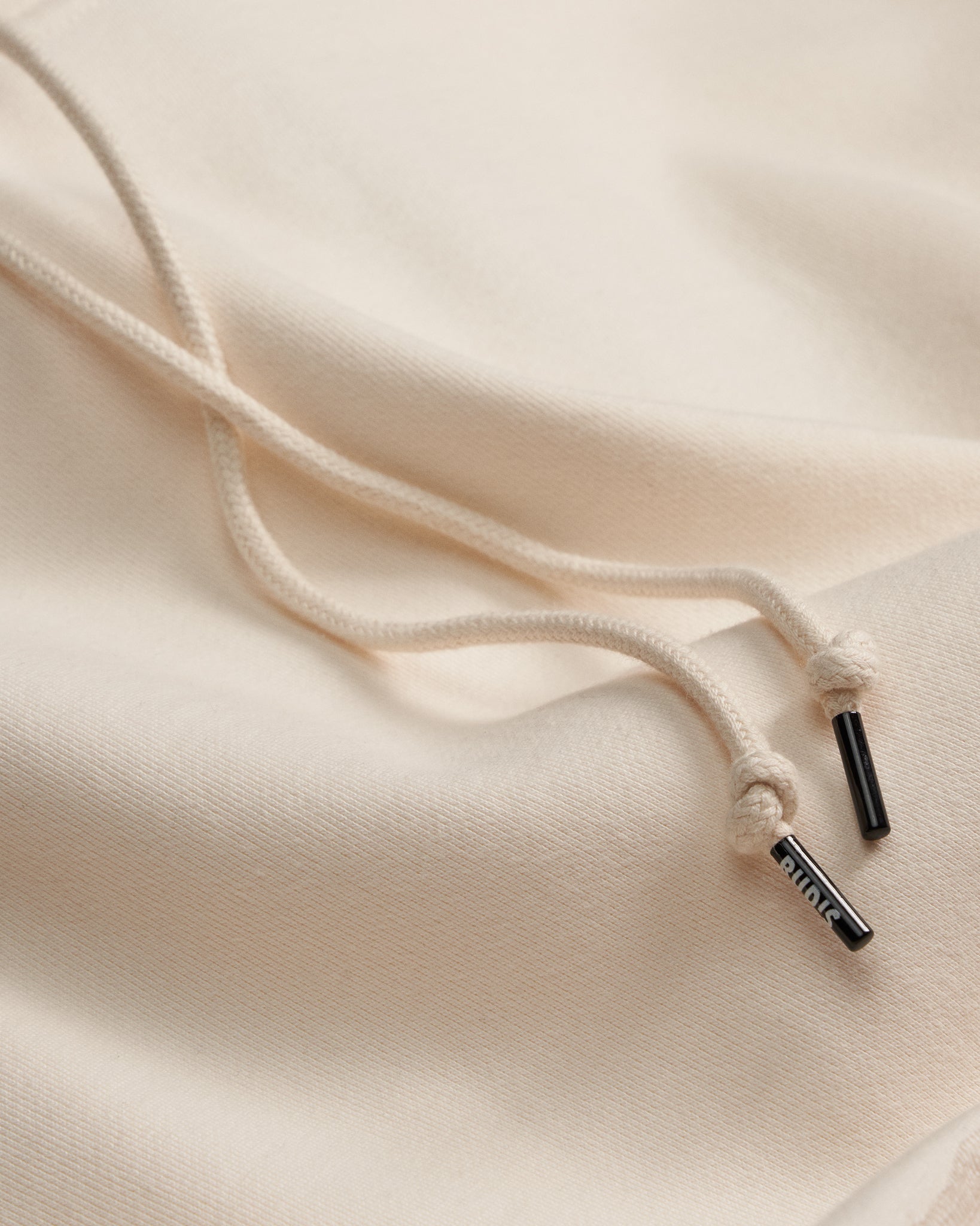 Close-up of a beige hoodie with a drawstring and brand logo on a beige background