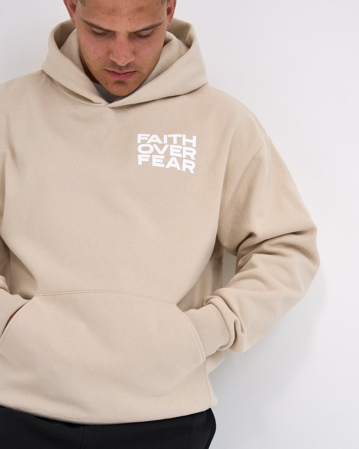 Beige hoodie with 'Faith Over Fear' text worn by a person on a white background