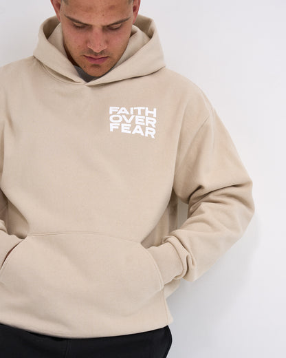 Beige hoodie with 'Faith Over Fear' text worn by a person on a white background