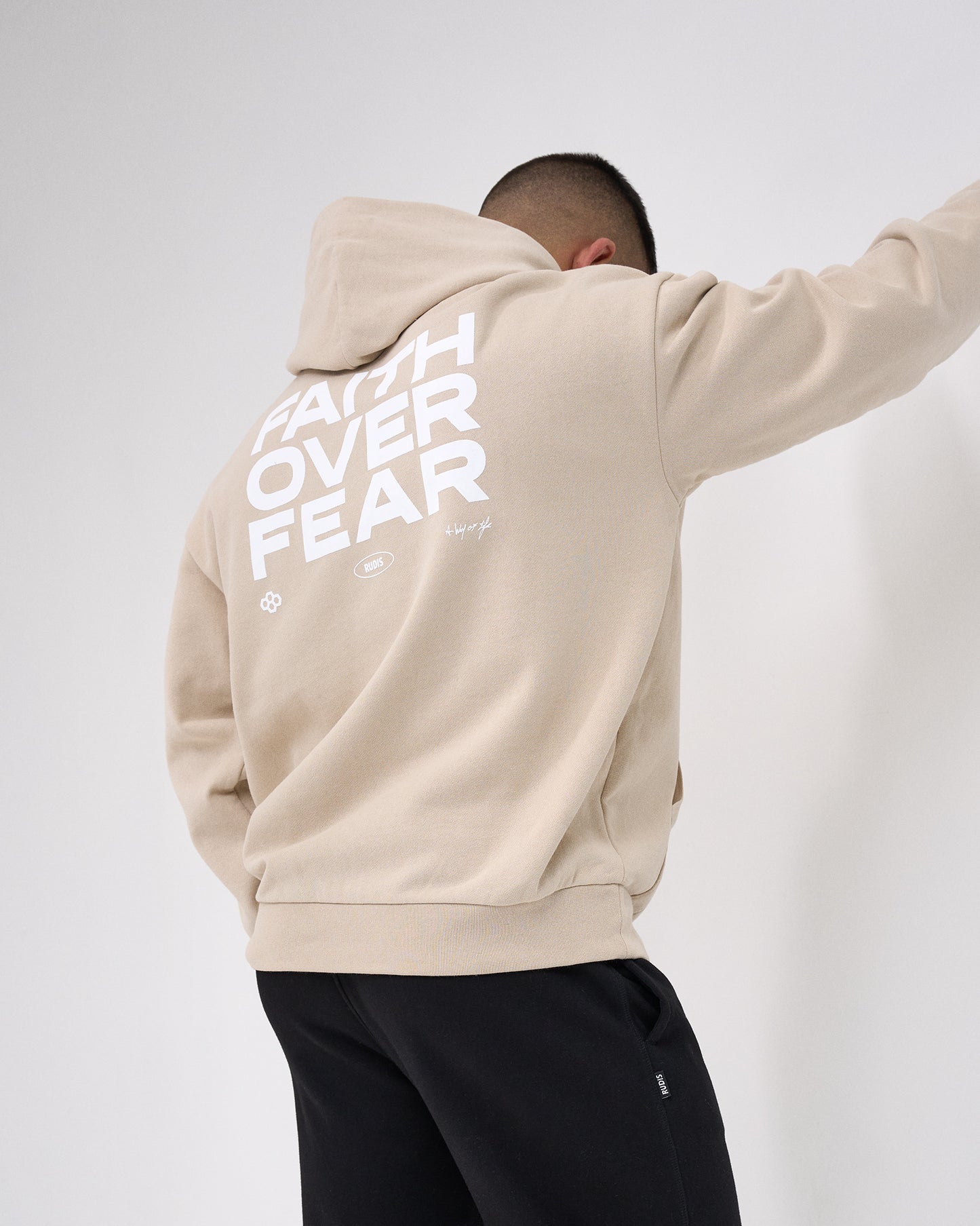 Person wearing a beige hoodie with 'Faith Over Fear' text on the back against a white background