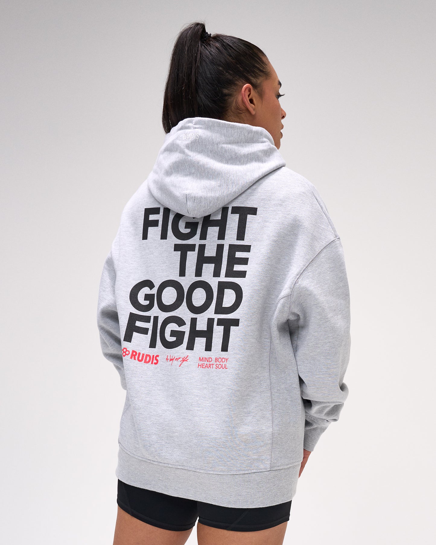 Person wearing a gray hoodie with 'Fight the Good Fight' text on the back, standing against a plain background.