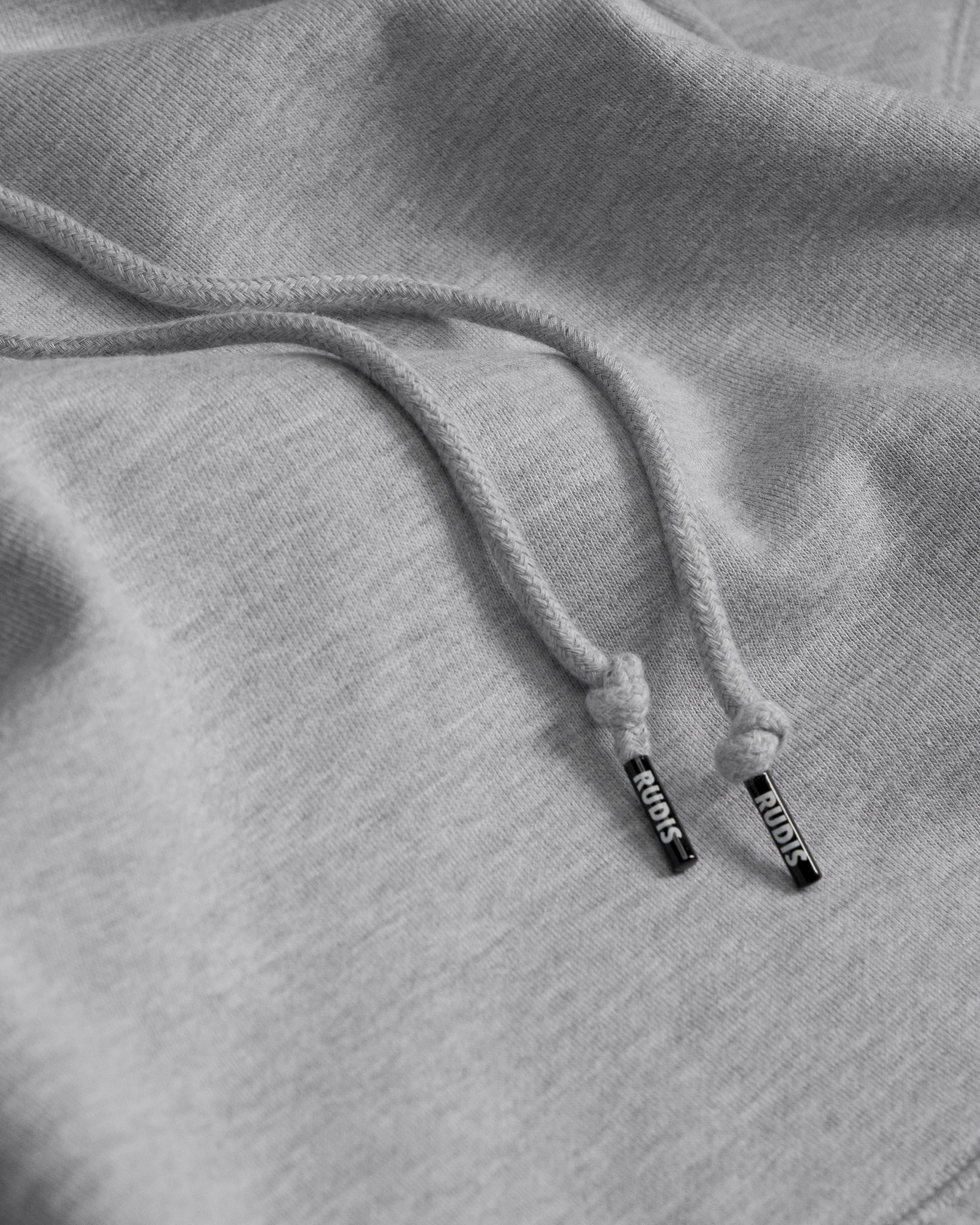 Close-up of gray hoodie with drawstring and 'RUDIS' brand logo on the aglet