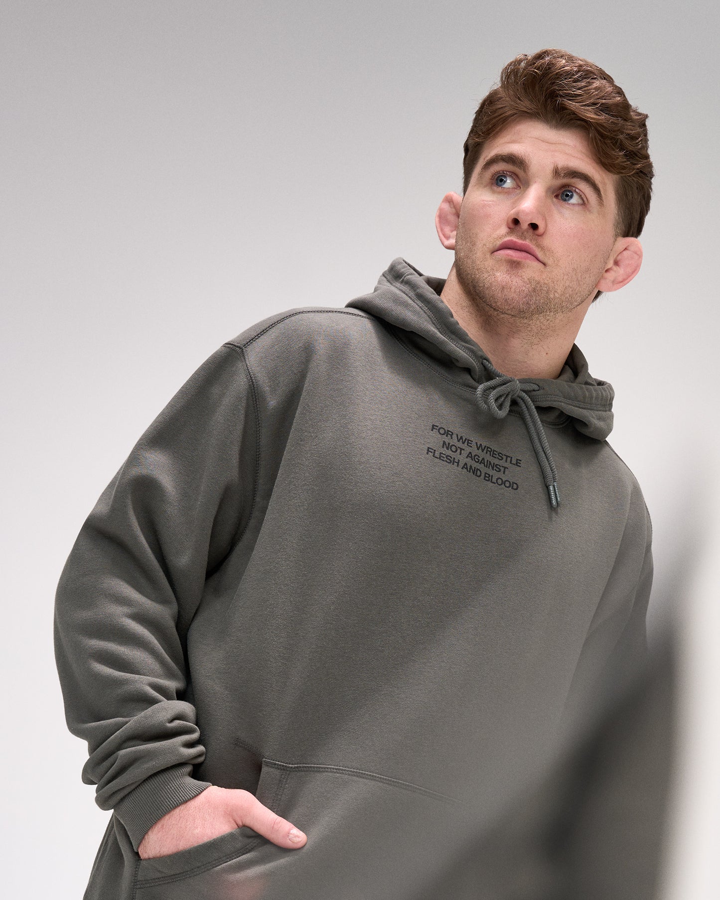 Man wearing a dark olive hoodie with text on the chest against a plain background