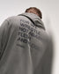 Person wearing a dark olive hoodie with 'For we wrestle not against flesh and blood' text and a brand logo on the back against a plain background