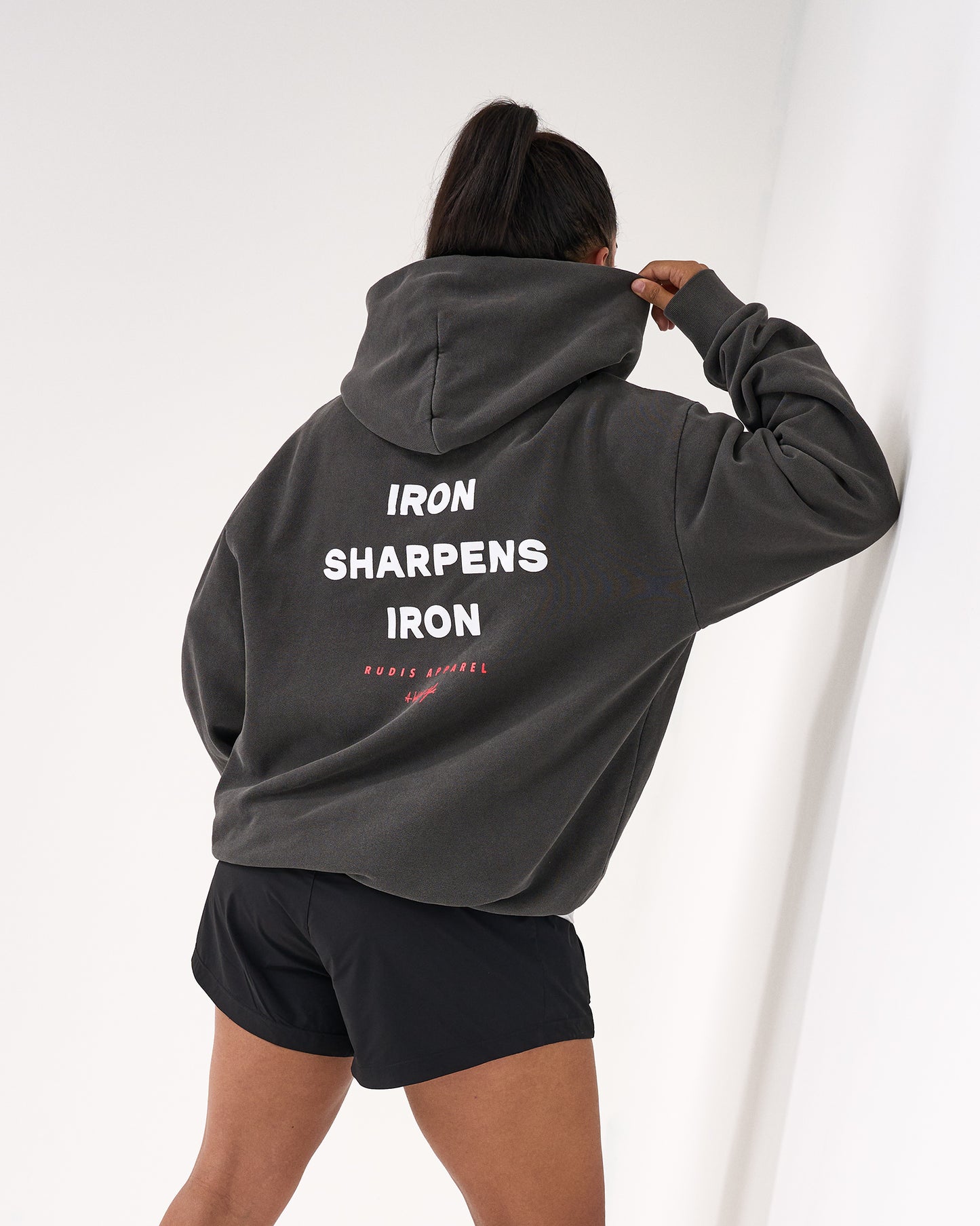 Person wearing a gray hoodie with 'IRON SHARPENS IRON' text on the back, standing against a white background.