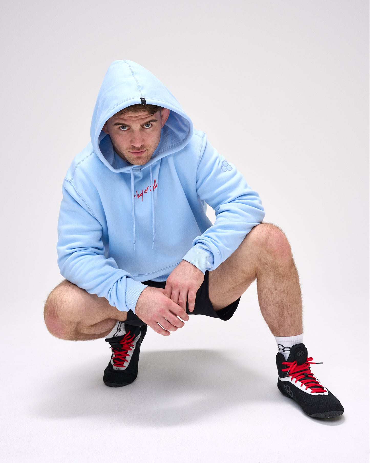 Person wearing a light blue hoodie and black sneakers with red accents on a white background