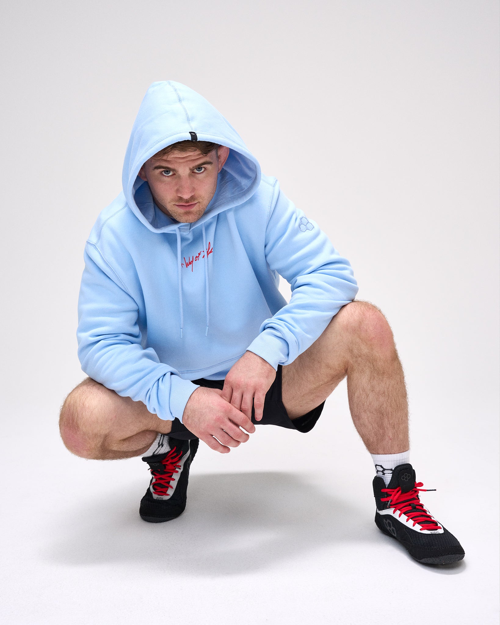 Person wearing a light blue hoodie and black sneakers with red accents on a white background