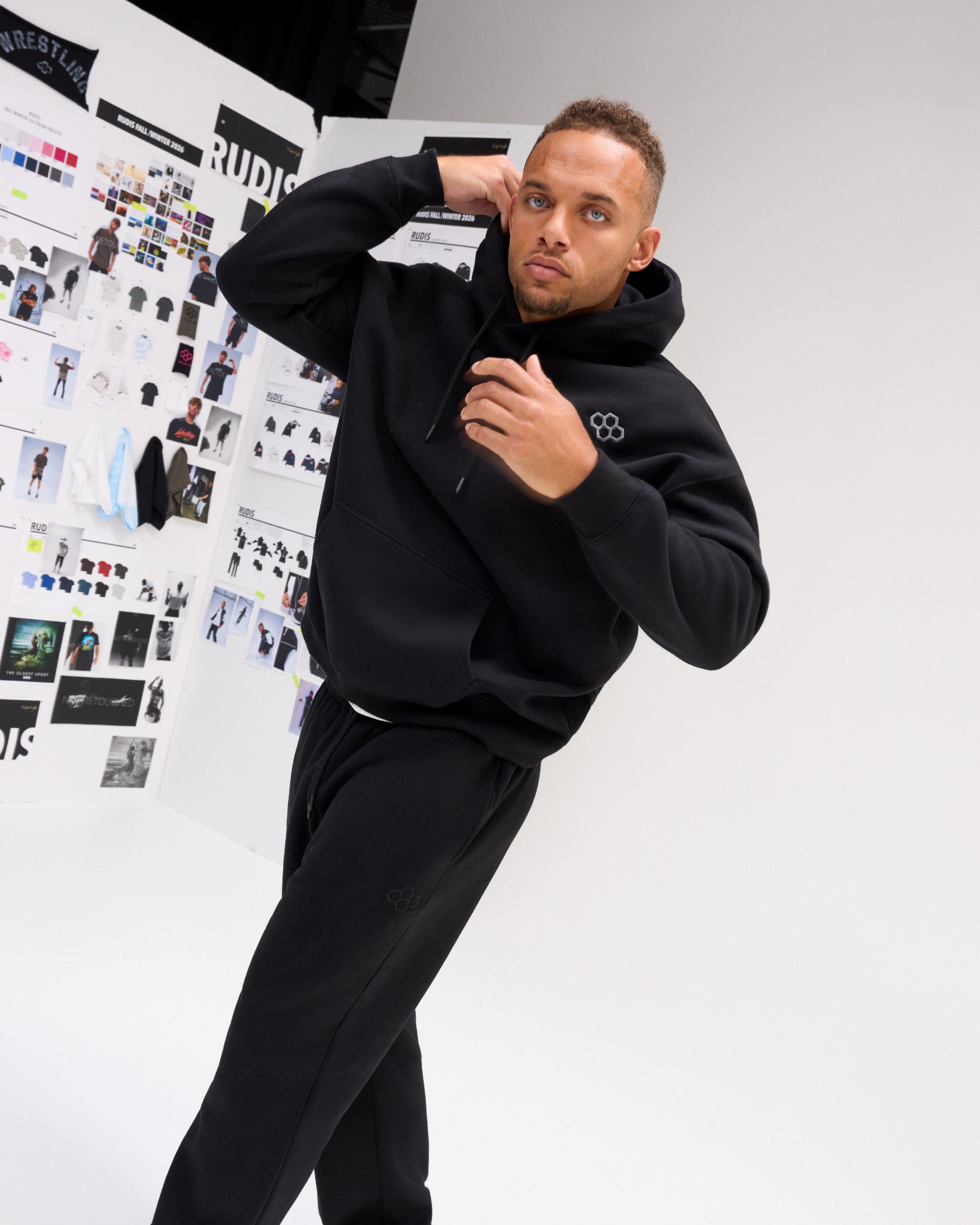 Male model wearing the black RUDIS Essential Hex Relaxed Comfort Fleece Hoodie with matching joggers, showing the relaxed fit and drawstring hood.