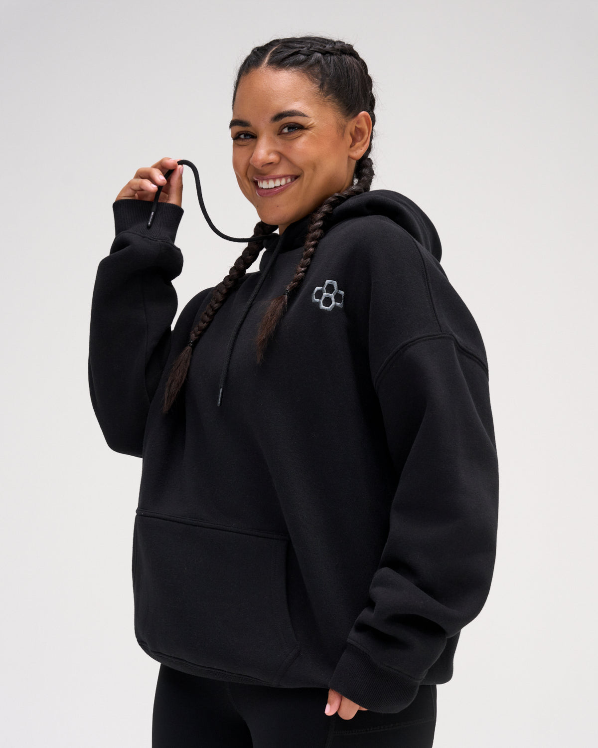 Female model wearing the RUDIS Essential Hex black fleece hoodie, highlighting the embroidered Hex logo, oversized sleeves and kangaroo pocket.