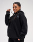 Female model wearing the RUDIS Essential Hex black fleece hoodie, highlighting the embroidered Hex logo, oversized sleeves and kangaroo pocket.