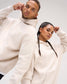 Male and female models wearing the RUDIS Essential Hex Relaxed Comfort Fleece Hoodie in Bone, featuring tonal Hex logos and drawstring hoods.