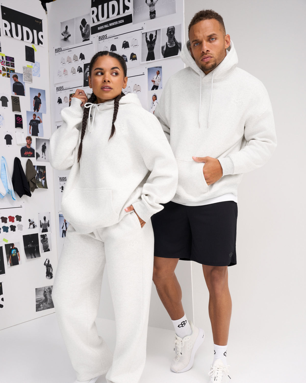 Male and female models wearing RUDIS Essential Hex Relaxed Comfort Fleece Hoodies in Heather Silver with tonal chest logos and matching athletic apparel.