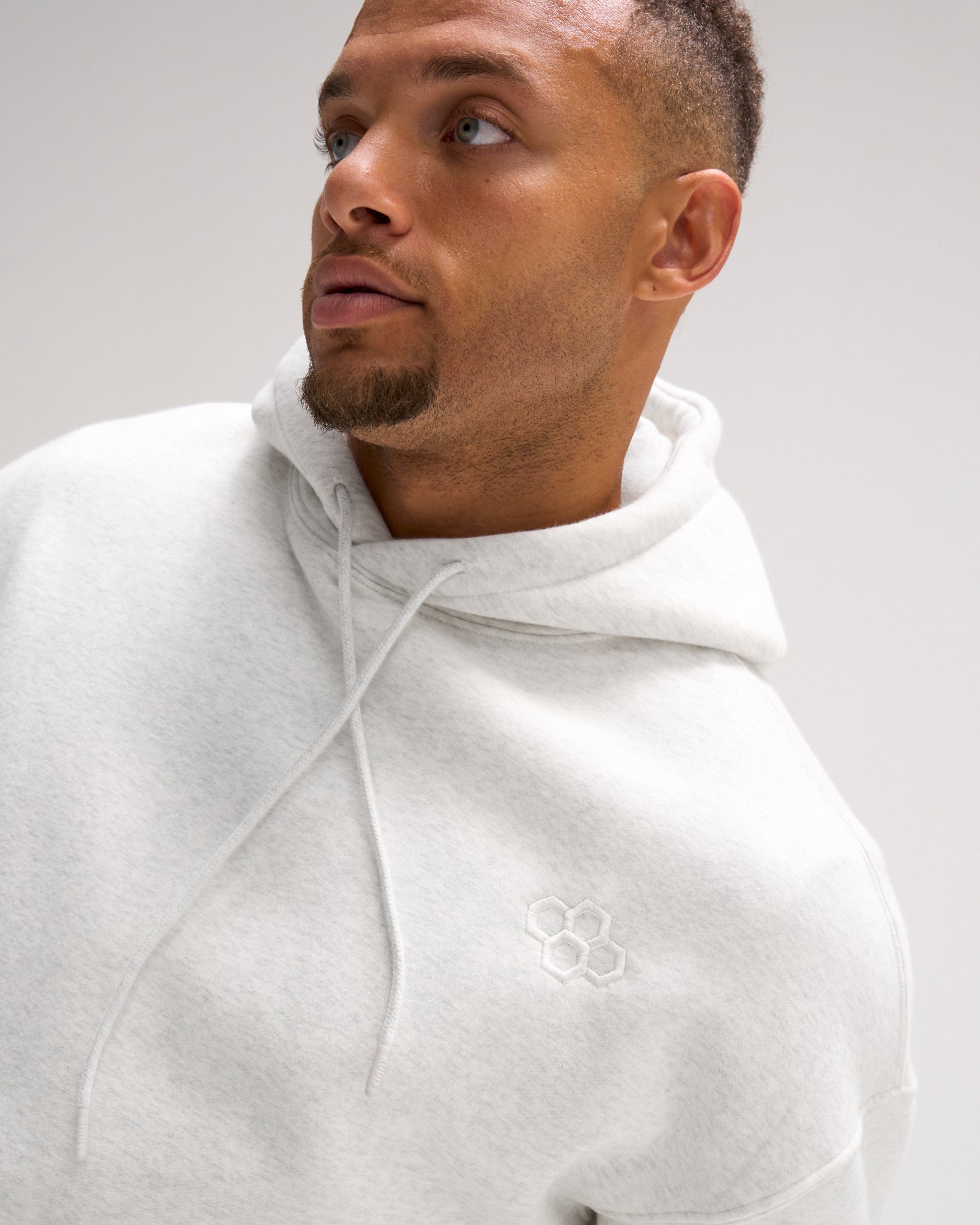 Close-up of a male model wearing the RUDIS Essential Hex fleece hoodie in Heather Silver, highlighting the tonal embroidered Hex logo and drawstring hood.