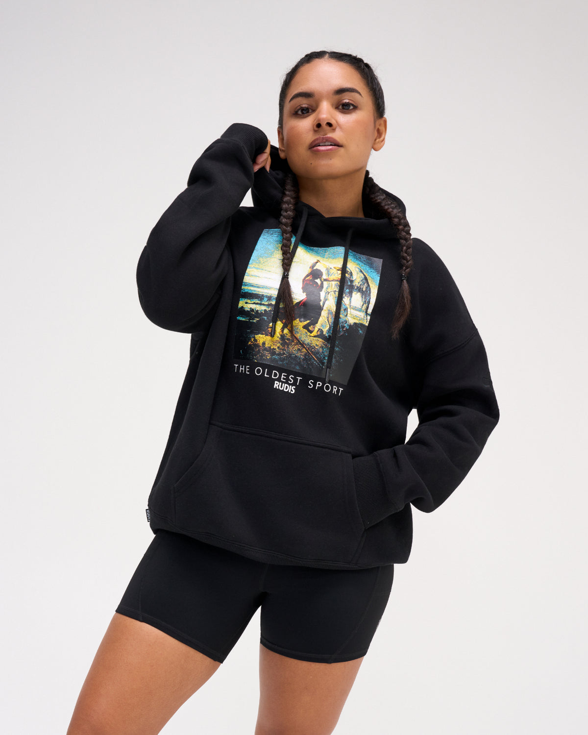 Female model wearing the RUDIS Divine Struggle fleece hoodie in Black with a relaxed fit, drawstring hood, kangaroo pocket and colorful front artwork.