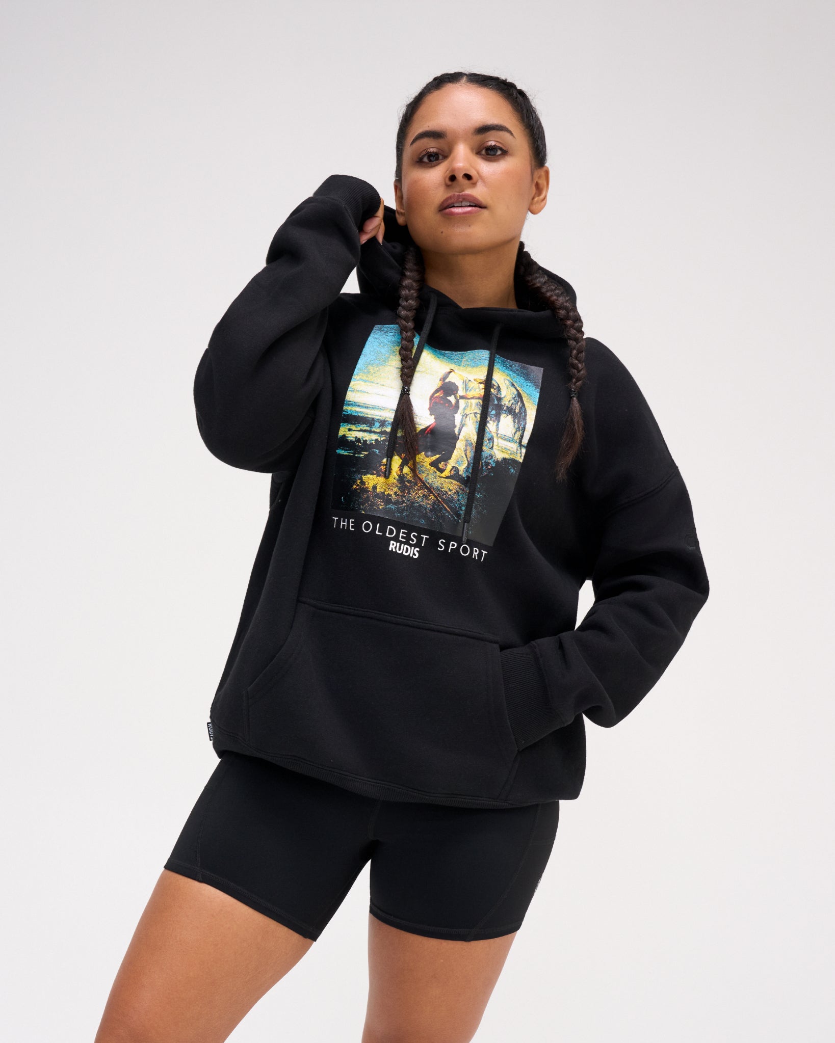 Female model wearing the RUDIS Divine Struggle fleece hoodie in Black with a relaxed fit, drawstring hood, kangaroo pocket and colorful front artwork.