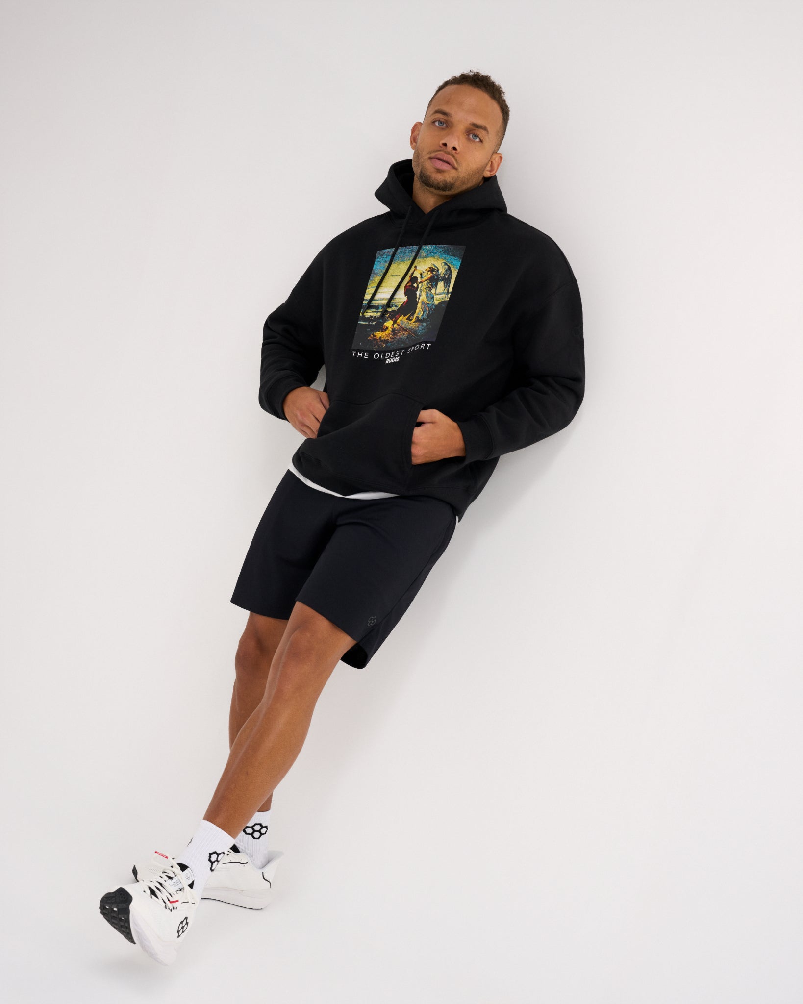 Male model wearing the RUDIS Divine Struggle Relaxed Comfort Fleece Hoodie in Black, showing the wrestling-inspired chest graphic and relaxed silhouette.