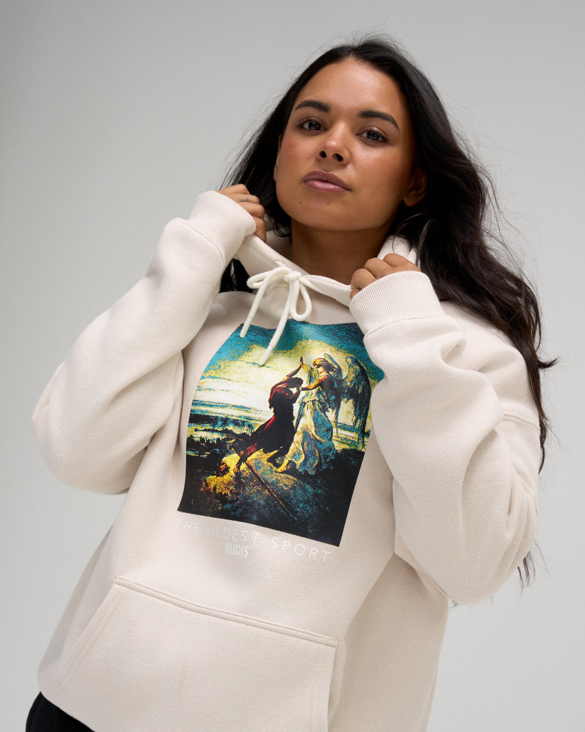 Female model wearing the RUDIS Divine Struggle Relaxed Comfort Fleece Hoodie in Bone, highlighting the oversized chest artwork and adjustable drawstring hood.