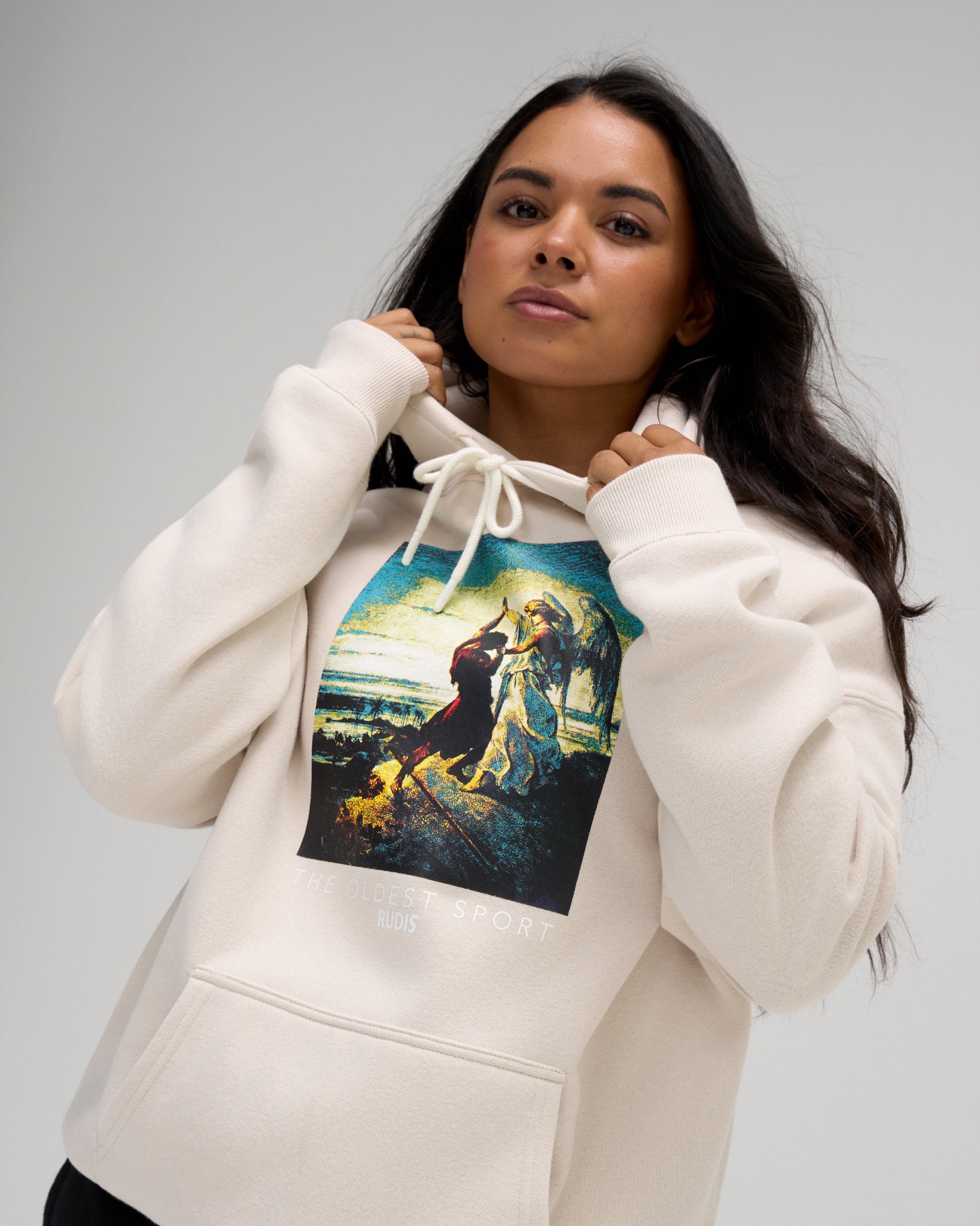 Female model wearing the RUDIS Divine Struggle Relaxed Comfort Fleece Hoodie in Bone, highlighting the oversized chest artwork and adjustable drawstring hood.