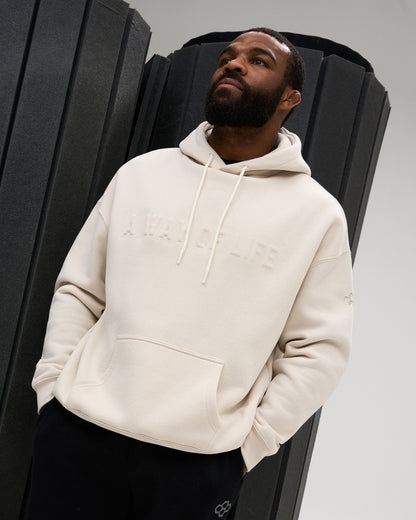 Male model wearing the RUDIS A Way Of Life Relaxed Comfort Fleece Hoodie in Bone, featuring tonal raised chest lettering, drawstring hood and front kangaroo pocket.