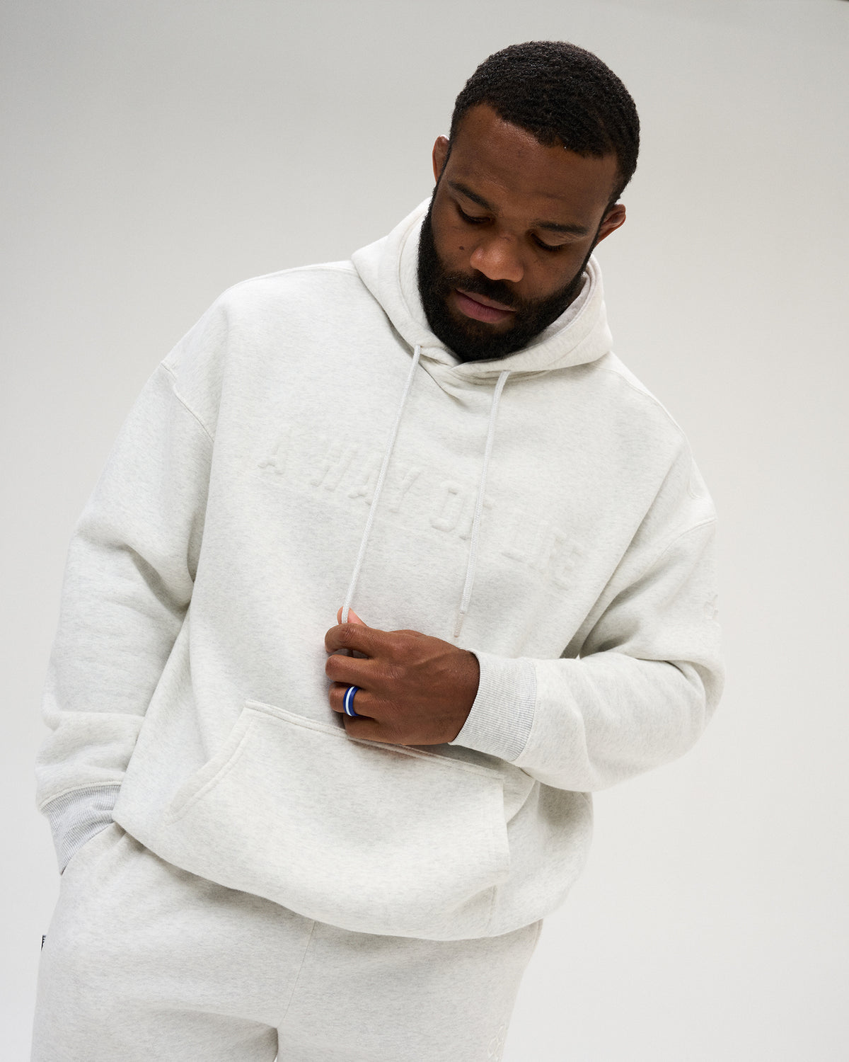 Front view of a male model wearing the RUDIS A Way Of Life Relaxed Comfort Fleece Hoodie in Heather Silver, showing tonal chest lettering, ribbed cuffs and relaxed fit.