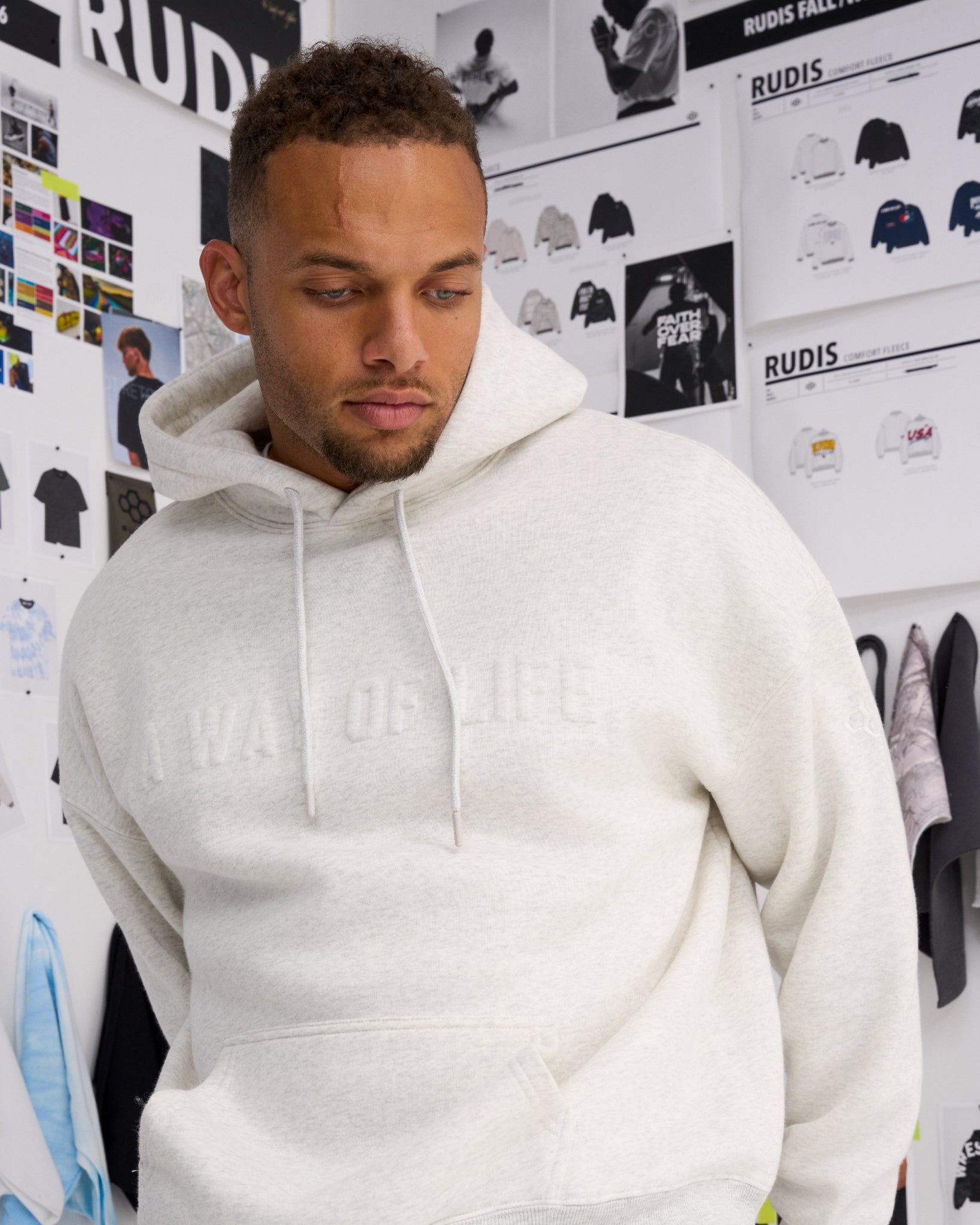 Close-up of a male model wearing the RUDIS A Way Of Life Relaxed Comfort Fleece Hoodie in Heather Silver, highlighting tonal raised lettering and drawstring hood.