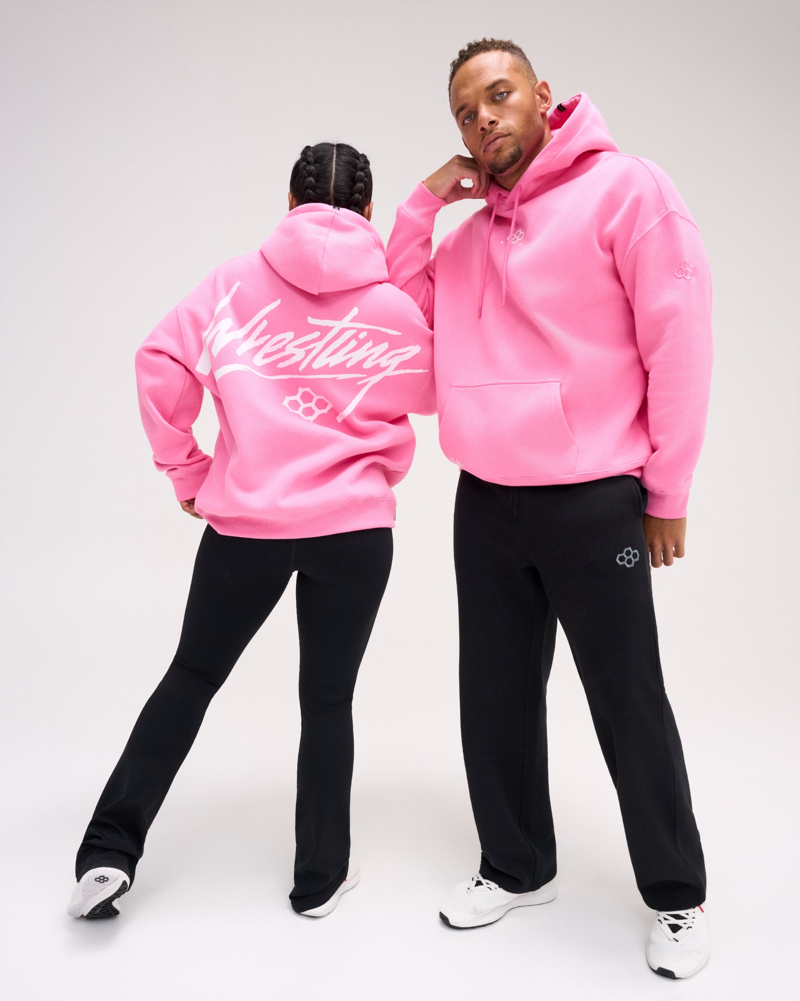 Male and female models wearing the RUDIS Art of Wrestling Relaxed Comfort Fleece Hoodie in Bubble Gum Pink, featuring a white Wrestling back graphic, drawstring hood and kangaroo pocket.