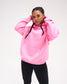 Female model wearing the RUDIS Art of Wrestling Relaxed Comfort Fleece Hoodie in Bubble Gum Pink, showing the relaxed fit, small white chest logo, drawstring hood and front kangaroo pocket.