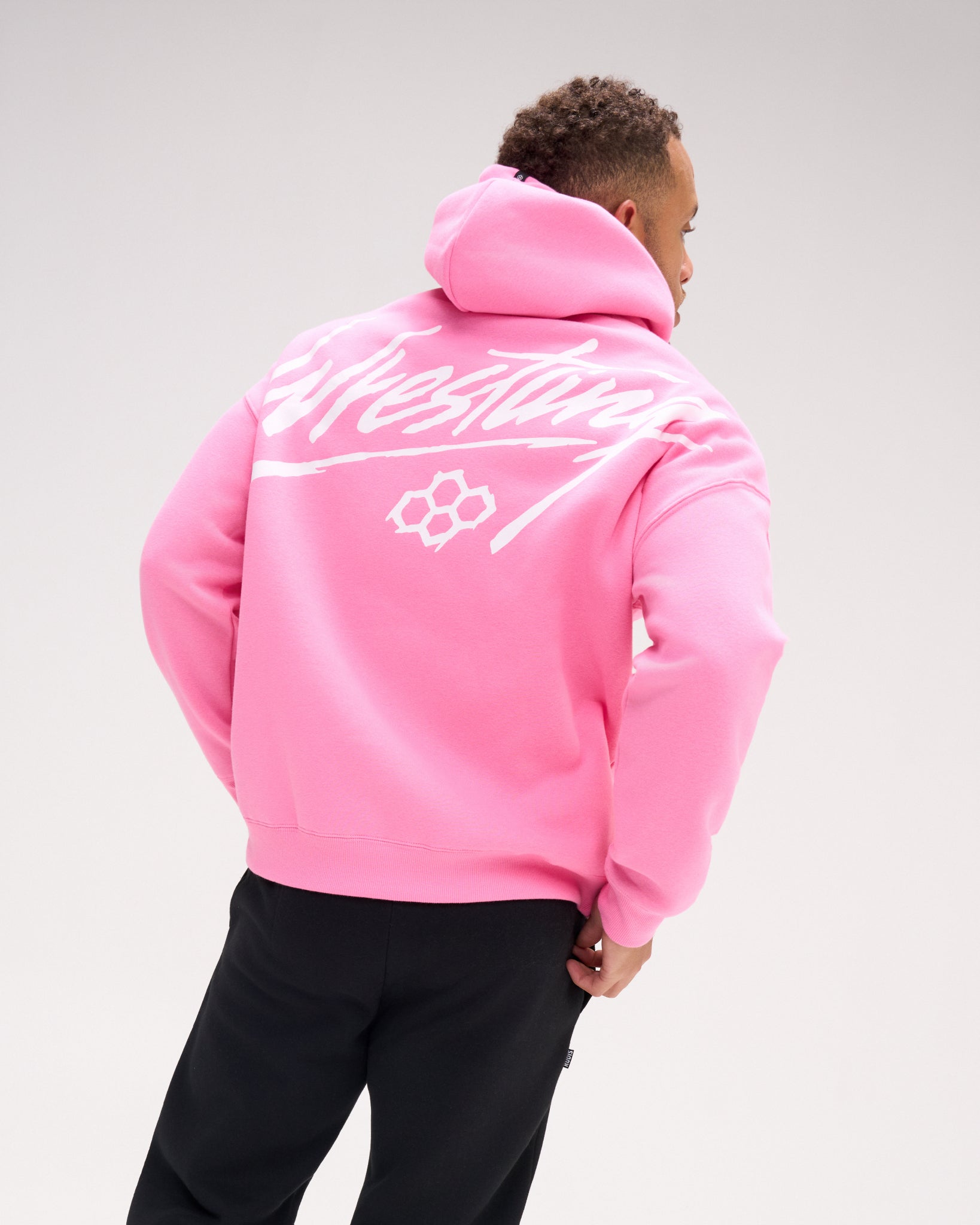 Back view of a male model wearing the RUDIS Art of Wrestling Relaxed Comfort Fleece Hoodie in Bubble Gum Pink, highlighting the oversized white Wrestling script graphic and RUDIS emblem.