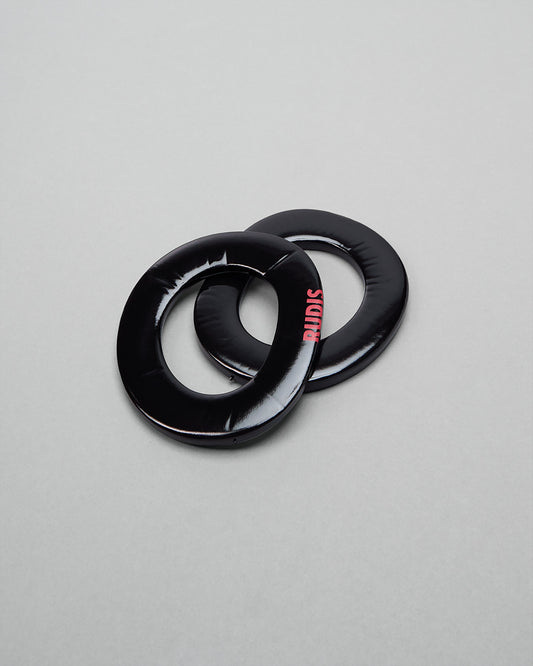 Two black wrestling headgear extension pads with 'RUDIS' branding on a gray background on a gray background