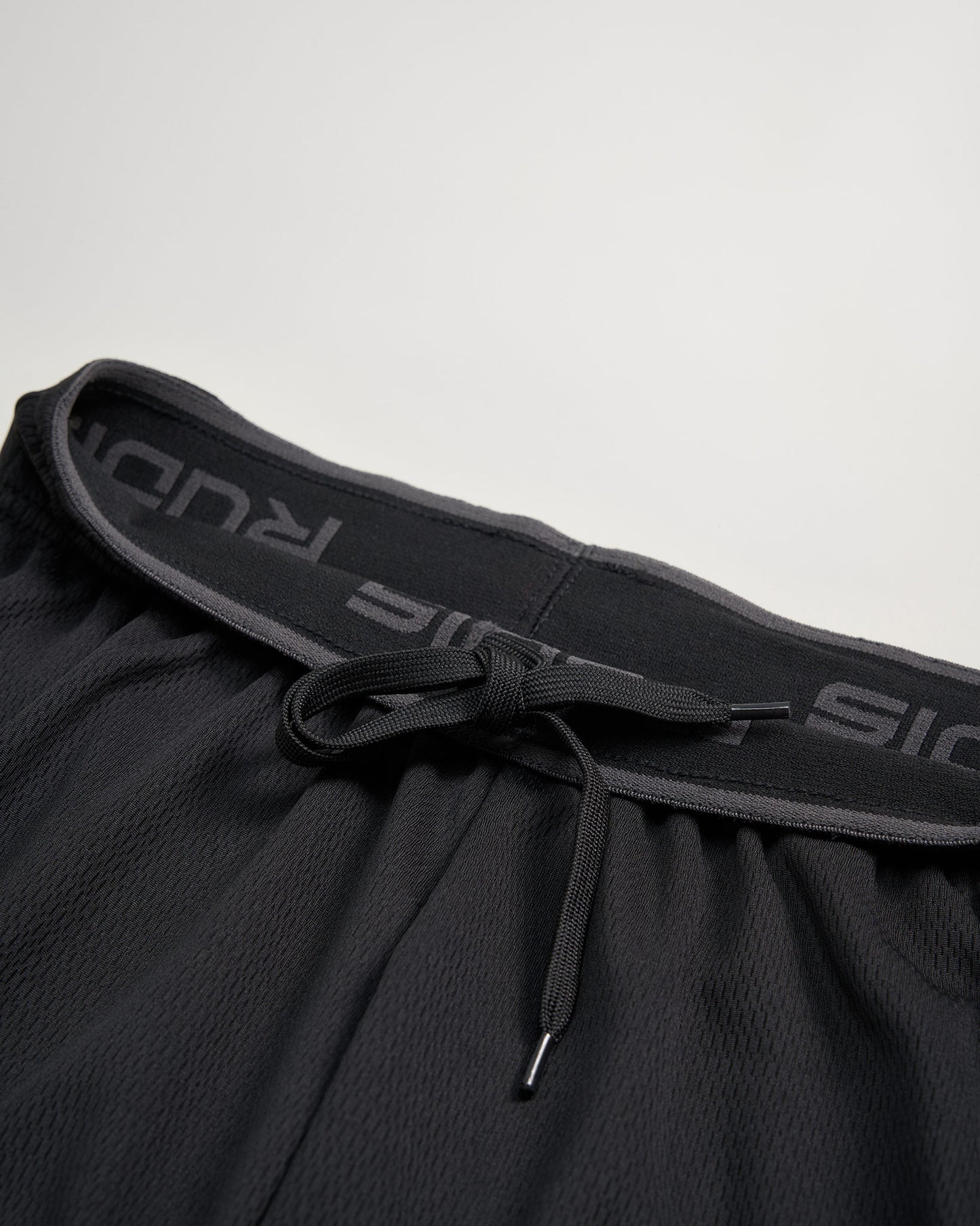 A close-up view of a black athletic short featuring a drawstring and a textured waistband