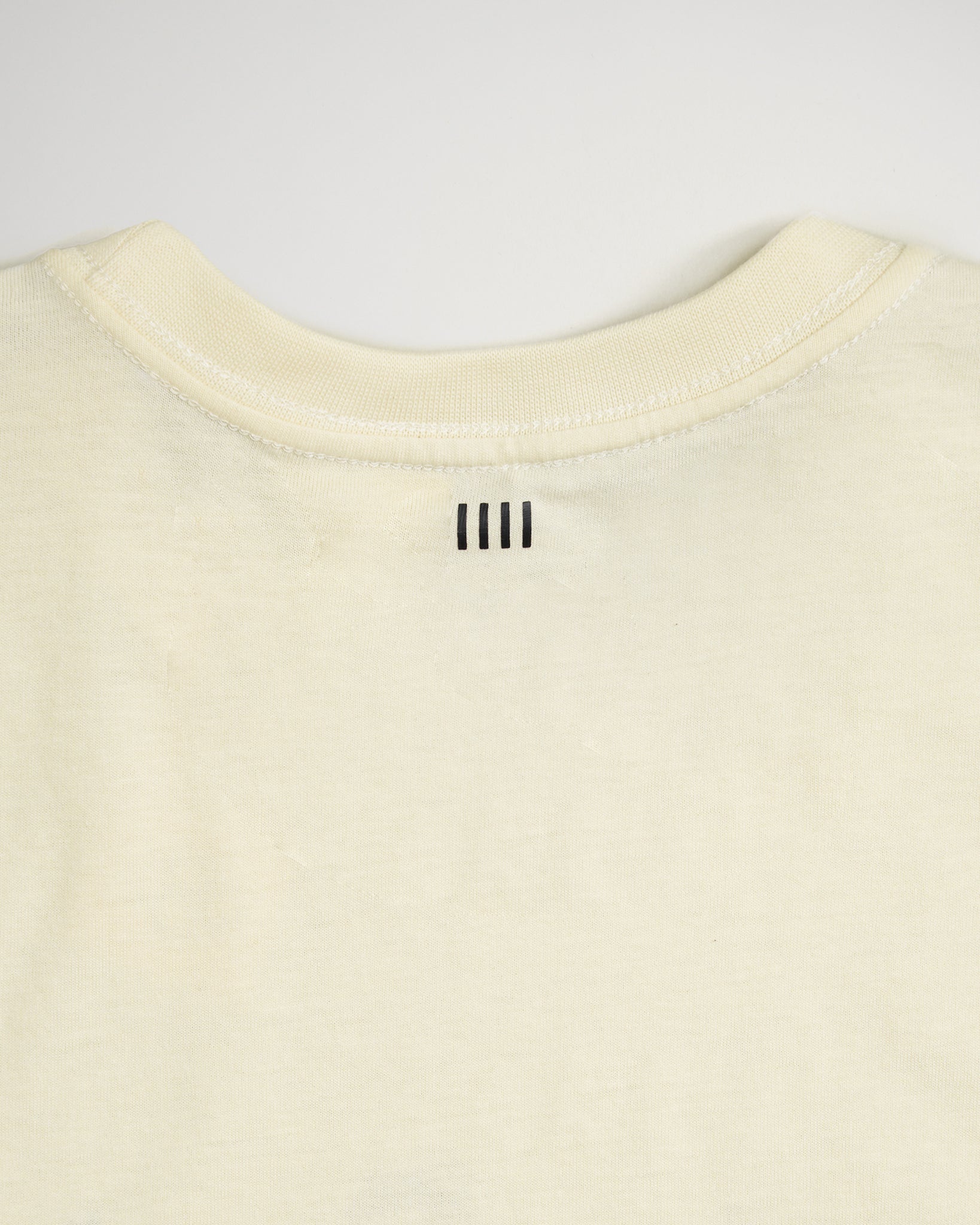 A close-up view of the back neckline of a light-colored shirt featuring three vertical black lines stitched at the center