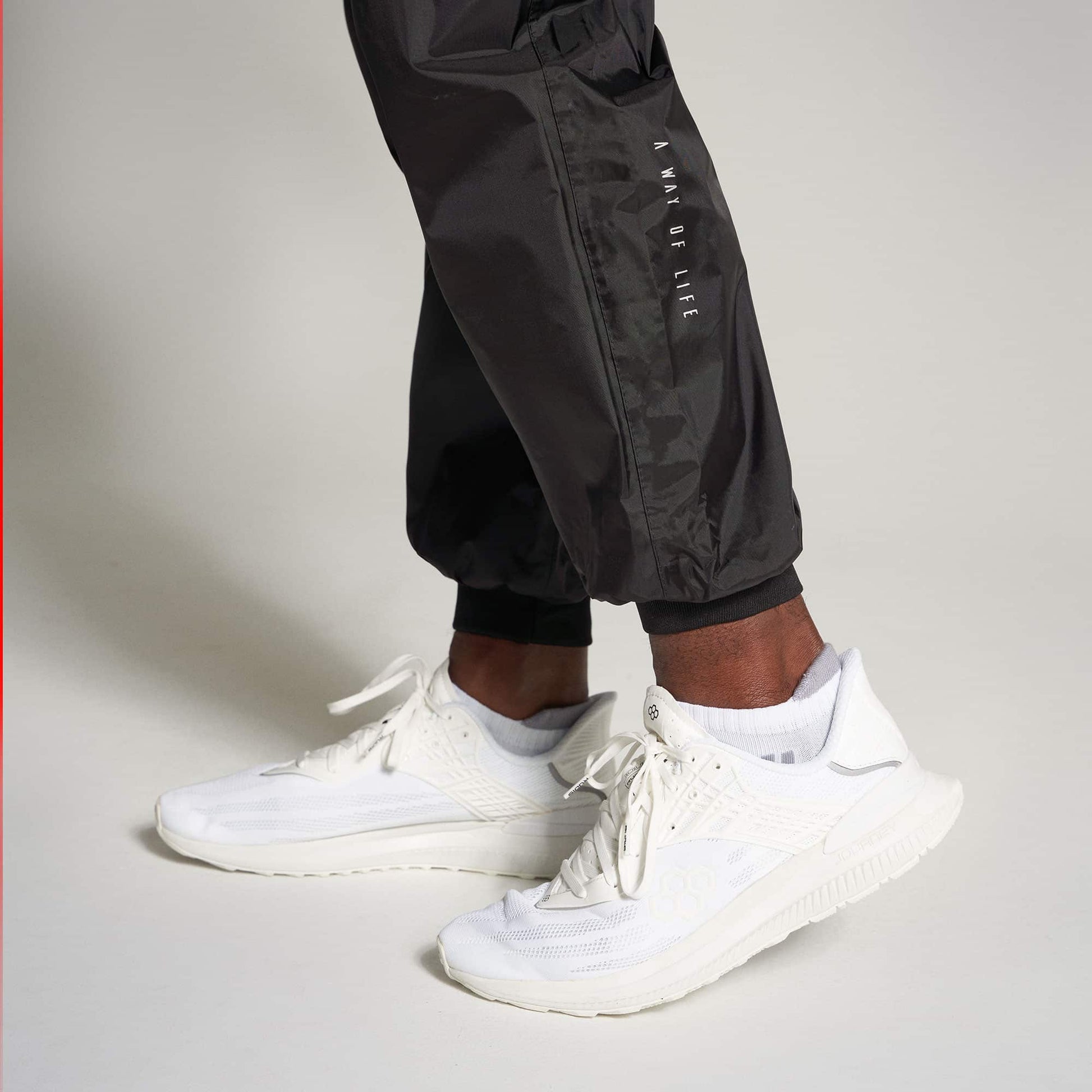 A close-up view of an individuals foot wearing white athletic shoes paired with black joggers highlighted against a neutral background