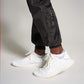 A close-up view of an individuals foot wearing white athletic shoes paired with black joggers highlighted against a neutral background