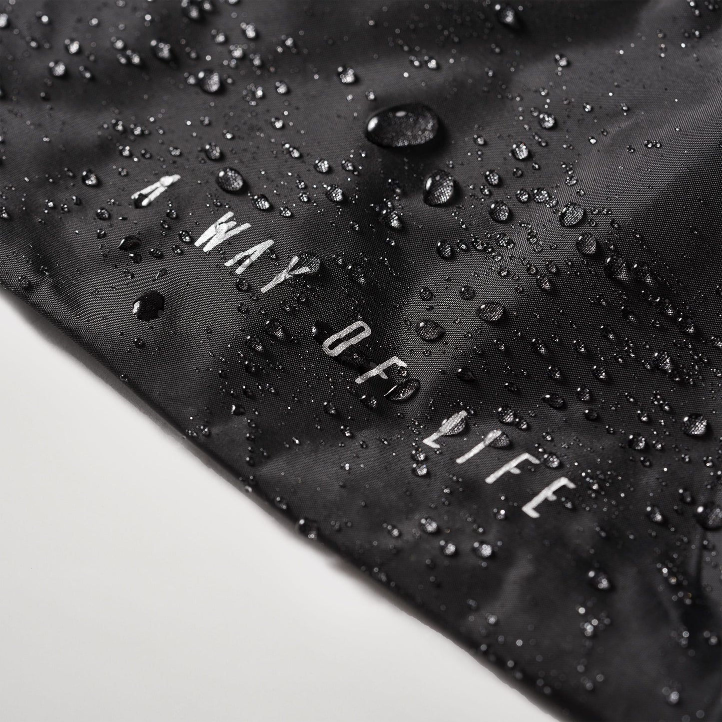 A close-up view of a black fabric with water droplets and the phrase A WAY OF LIFE printed in white
