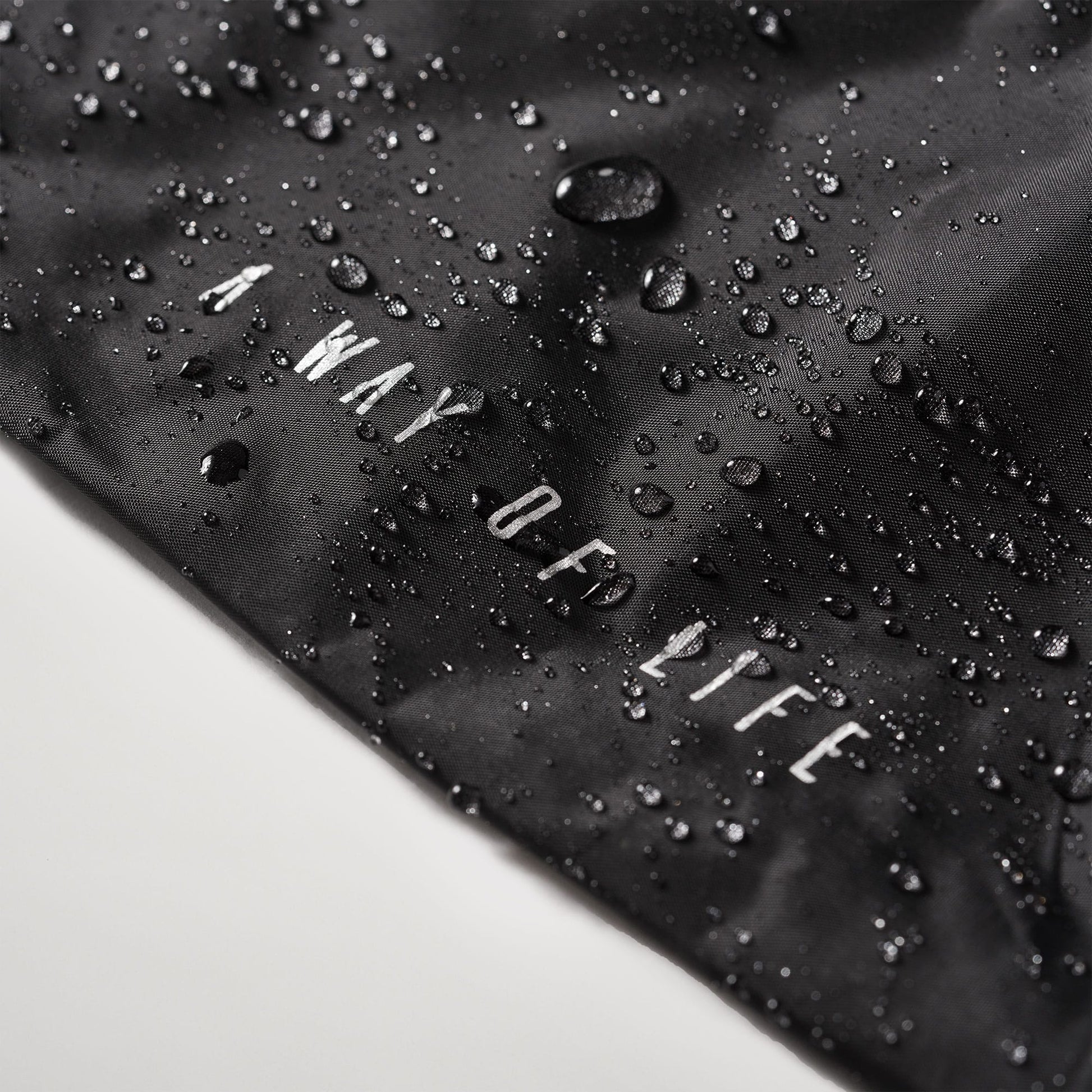 A close-up view of a black fabric with water droplets and the phrase A WAY OF LIFE printed in white