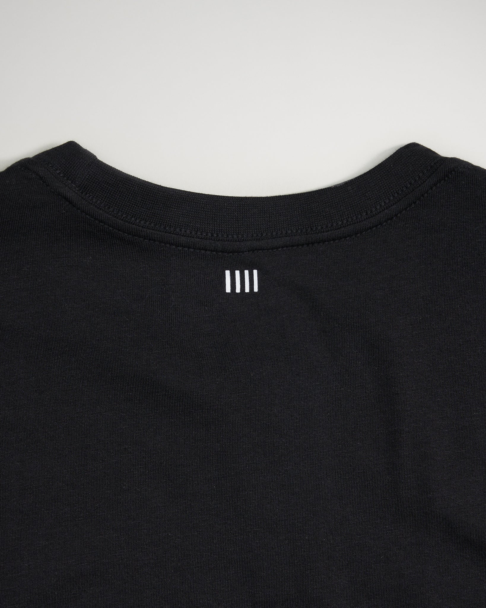 A close-up view of the back neckline of a black T-shirt featuring two white horizontal stripes and a minimalistic design