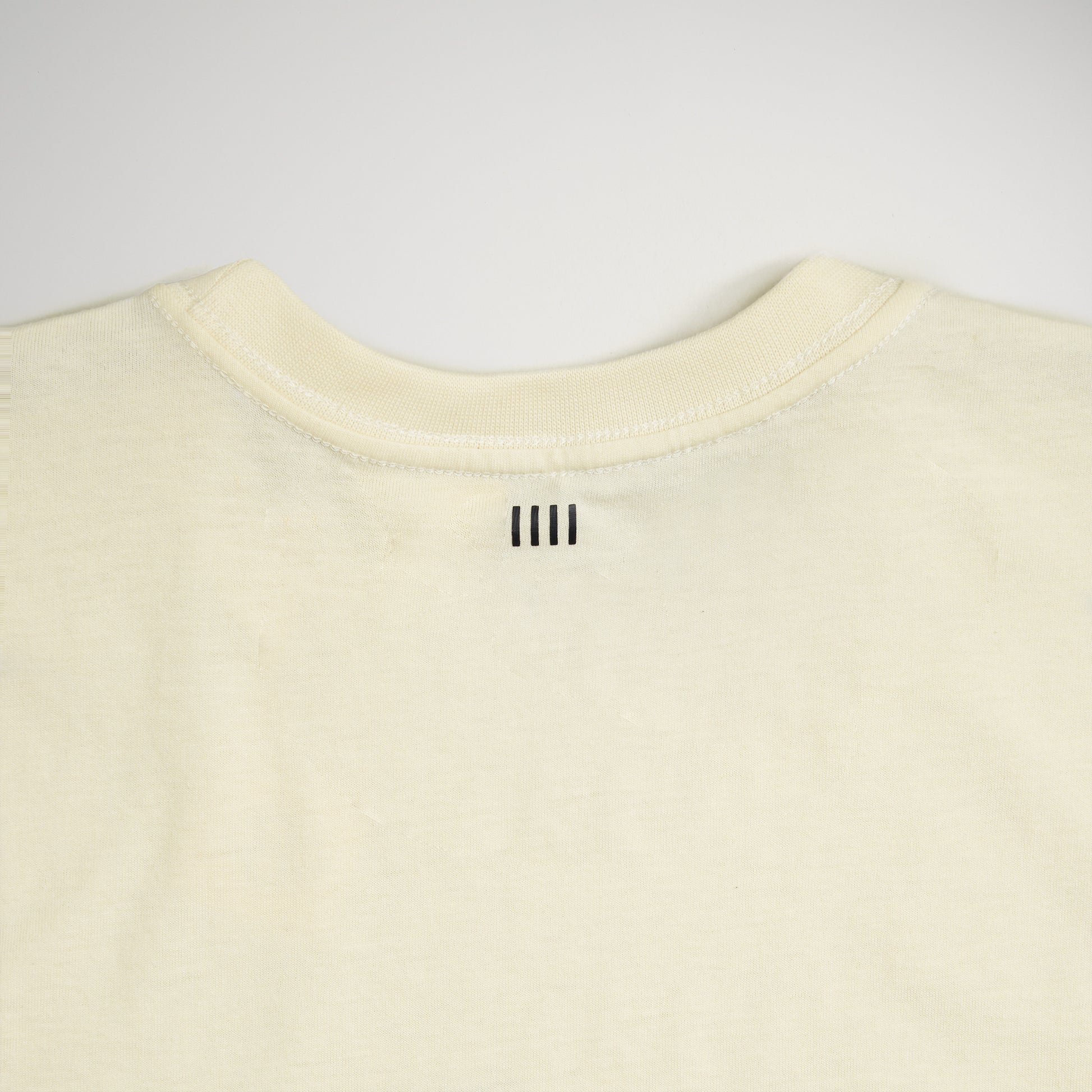 A plain cream-colored t-shirt featuring a subtle minimalistic design element on the back neckline