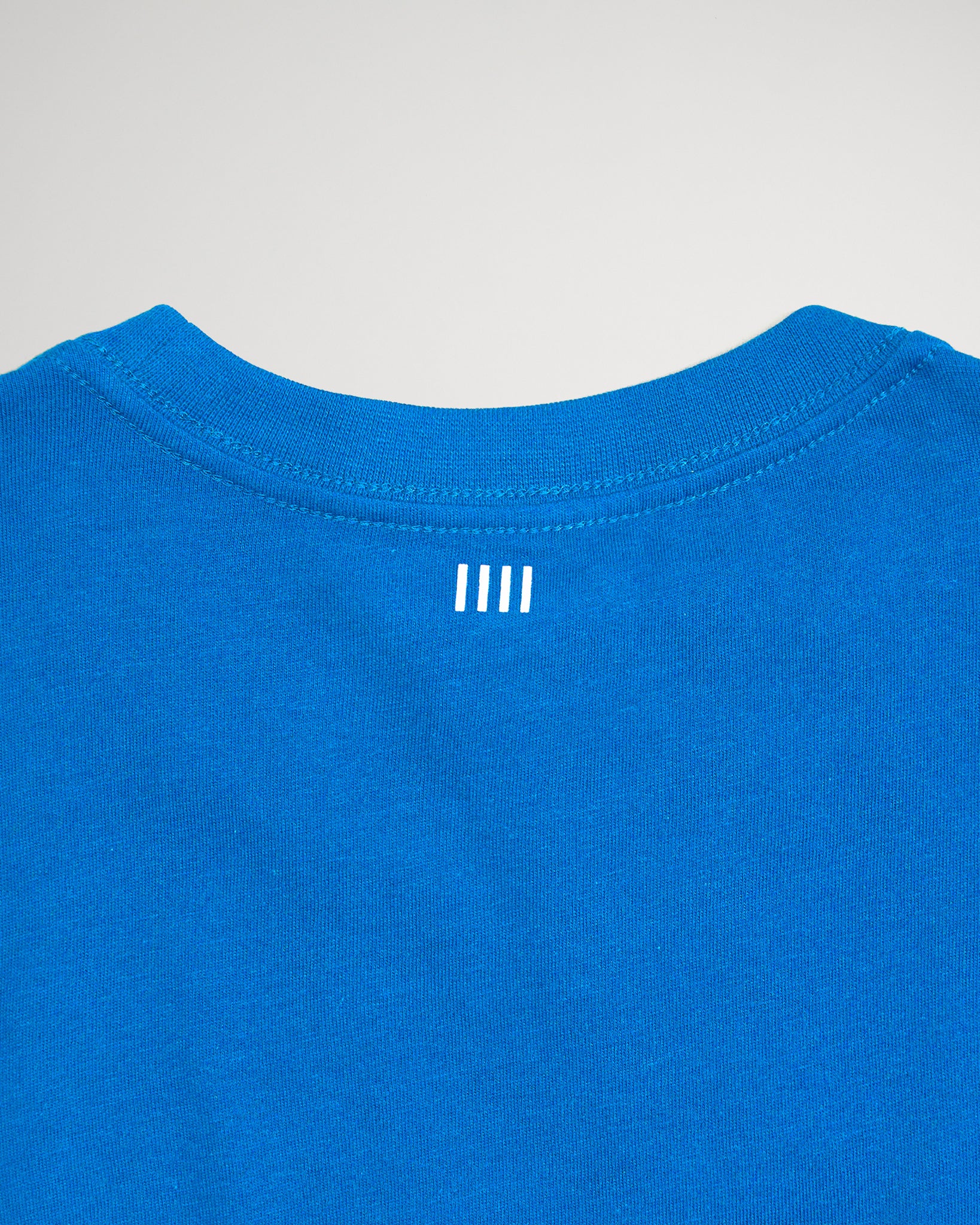 The image features the back of a vibrant blue t-shirt highlighting a minimalist design with three vertical white stripes near the neckline